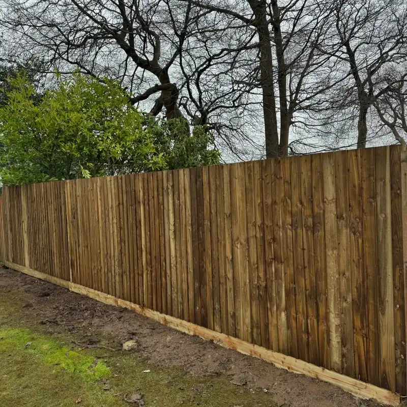 New feather edge fence around the side of a lawn, with trees and a house beyond